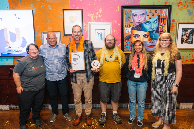 The ProWorks team in Chicago, wearing feather boas, accepting The Stars, Stripes & AI award from Brad Rockwood of Umbraco HQ in 2026